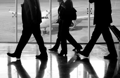 shadows of a group of business people walking in an airport. There is a plane in the background.
